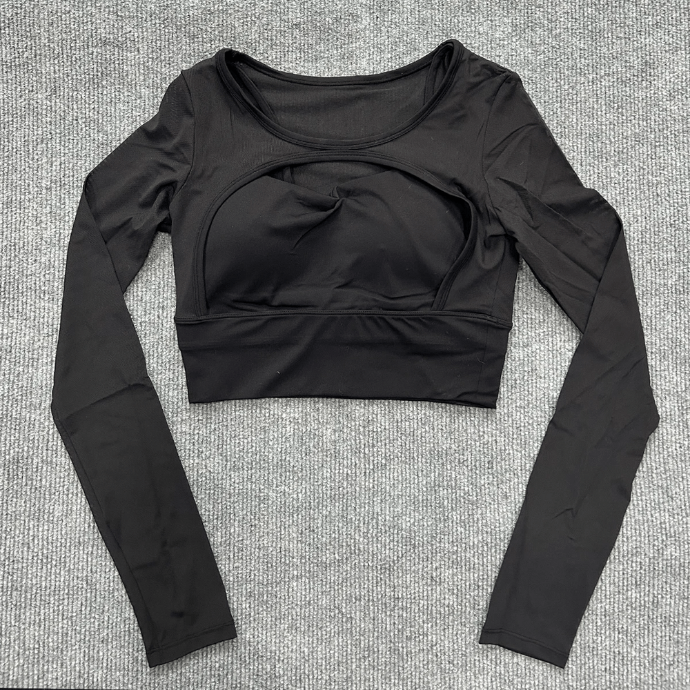 Black women's quick dry mesh yoga crop top with long sleeves and chest pads on a textured surface.